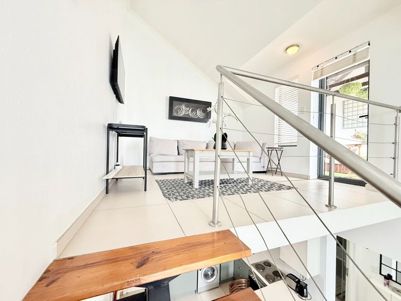 An open-plan living area featuring a vaulted ceiling, tiled floors, and a modern stainless steel balustrade overlooking the lower level.