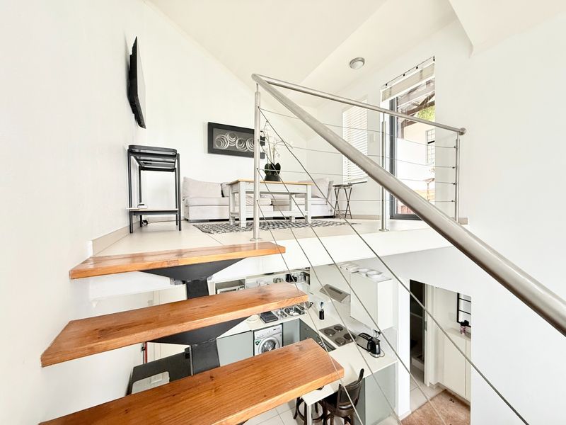 Open-plan split-level apartment featuring a modern staircase with stainless steel railings, overlooking a functional kitchen area with built-in cabinetry and appliances.
