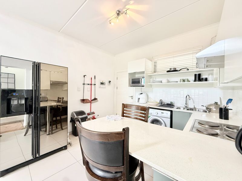 A functional kitchen featuring stone countertops, built-in cabinetry, an electric hob with extractor fan, and an integrated washing machine.
