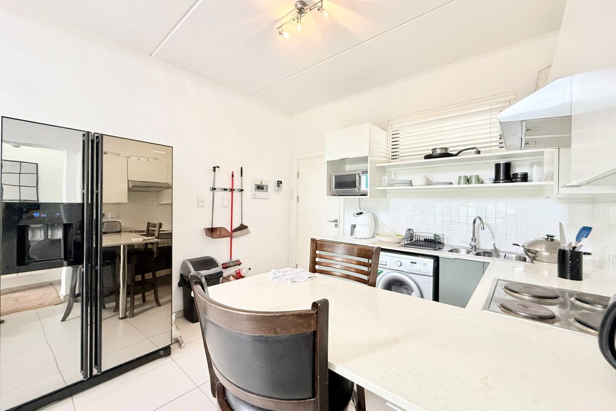 A functional kitchen featuring stone countertops, built-in cabinetry, an electric hob with extractor fan, and an integrated washing machine.