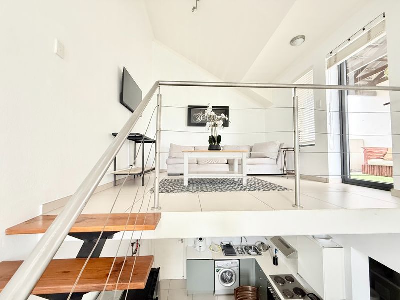 Open-plan apartment layout featuring a mezzanine living area with stainless steel balustrades overlooking a compact kitchen with built-in appliances and tiled flooring.