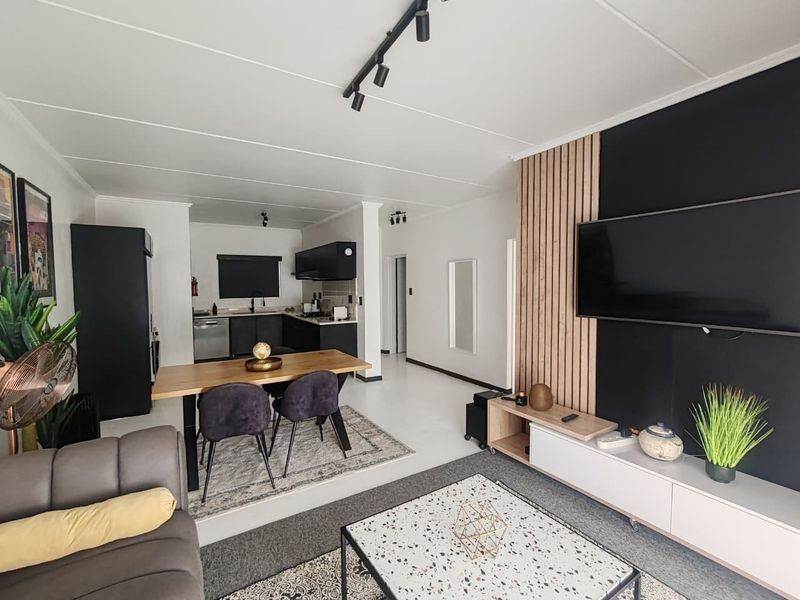 Modern open-plan living and kitchen area featuring contemporary finishes, track lighting, and a stylish timber slat feature wall.