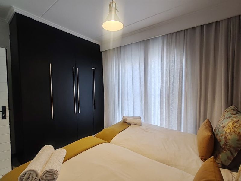 A well-maintained bedroom featuring modern dark built-in cupboards and floor-to-ceiling window treatments.