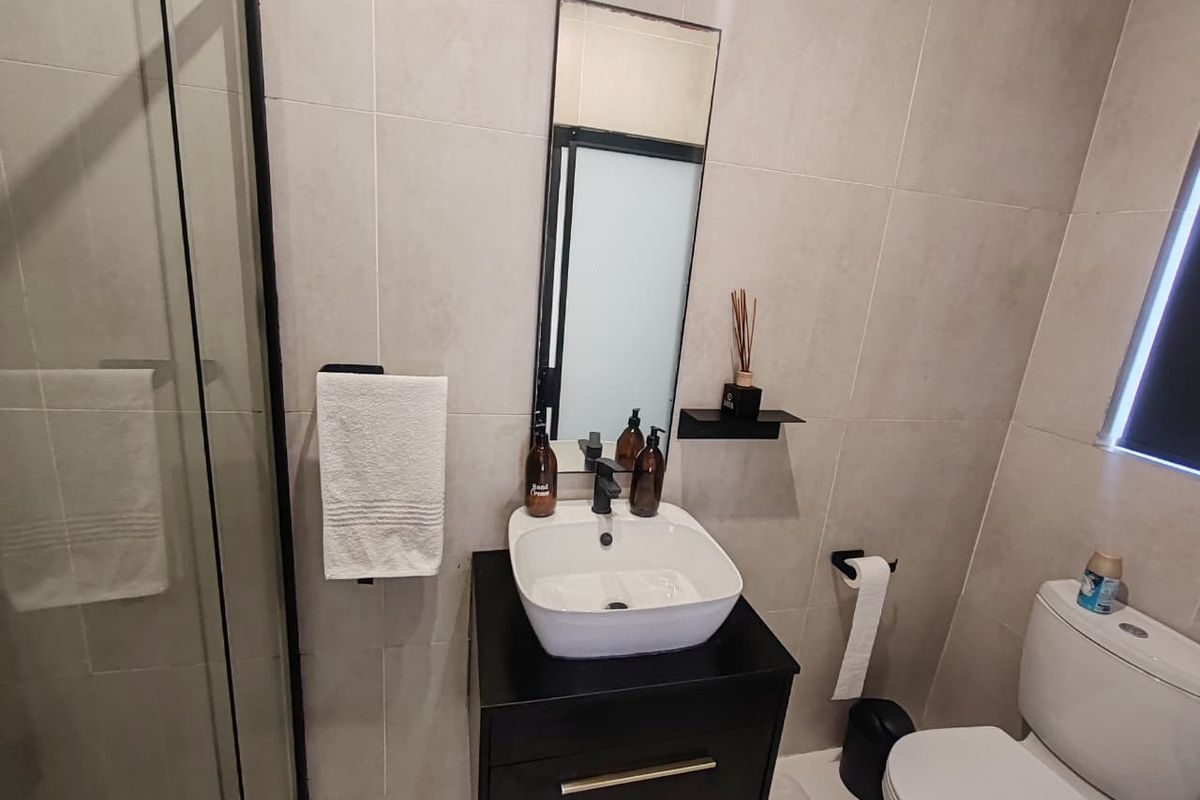 Modern bathroom featuring a vessel sink on a black vanity, a glass shower enclosure, and neutral wall tiling.
