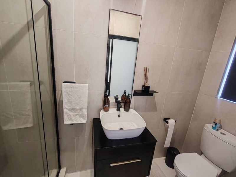 Modern bathroom featuring a vessel sink on a black vanity, a glass shower enclosure, and neutral wall tiling.