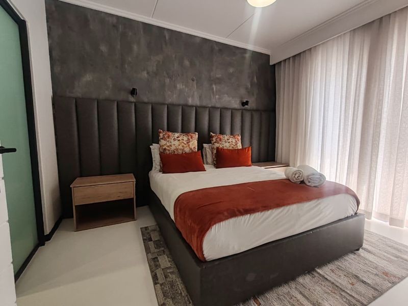 A modern bedroom featuring a large upholstered headboard, a textured feature wall, and floor-to-ceiling curtains.