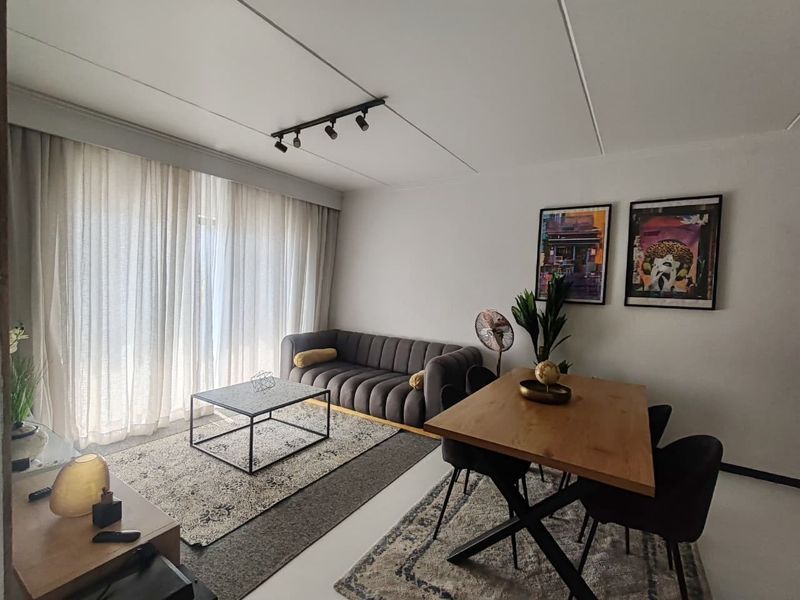 A bright open-plan living and dining area featuring modern track lighting and large windows with floor-to-ceiling curtains.