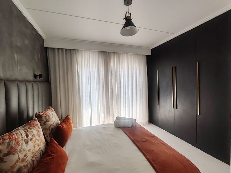 Modern bedroom featuring sleek floor-to-ceiling built-in cupboards with gold handles, an upholstered headboard, and elegant sheer curtains.