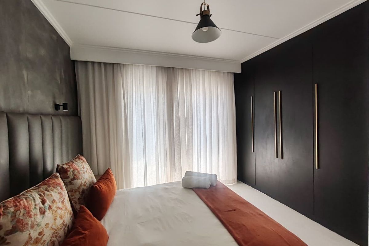 Modern bedroom featuring sleek floor-to-ceiling built-in cupboards with gold handles, an upholstered headboard, and elegant sheer curtains.
