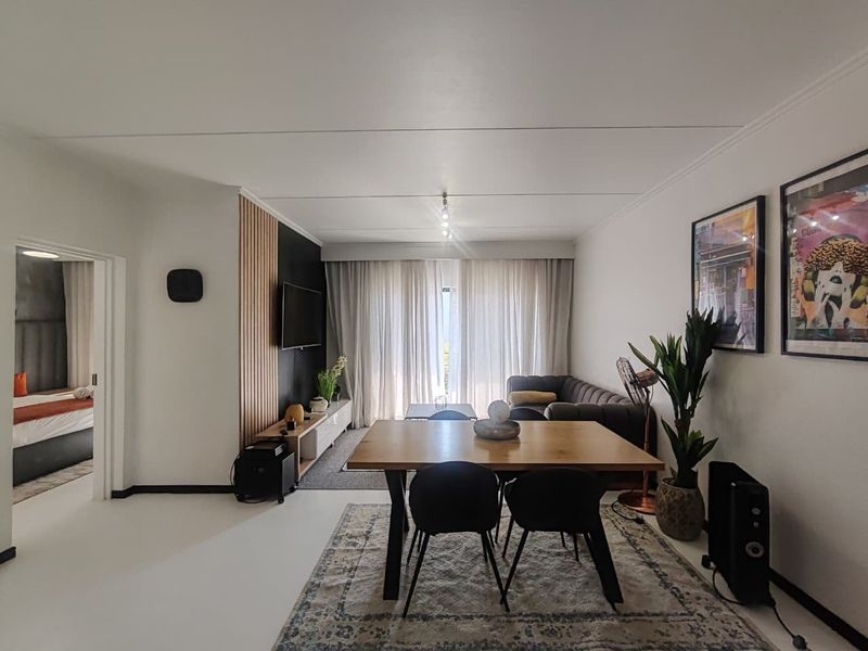 Modern open-plan living and dining area featuring a stylish slatted timber accent wall, neutral flooring, and ample natural light through floor-to-ceiling curtains.