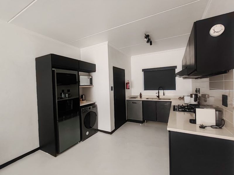 Modern kitchen featuring sleek black cabinetry, stone countertops, a gas hob, extractor fan, and integrated sink with a contemporary mixer tap.