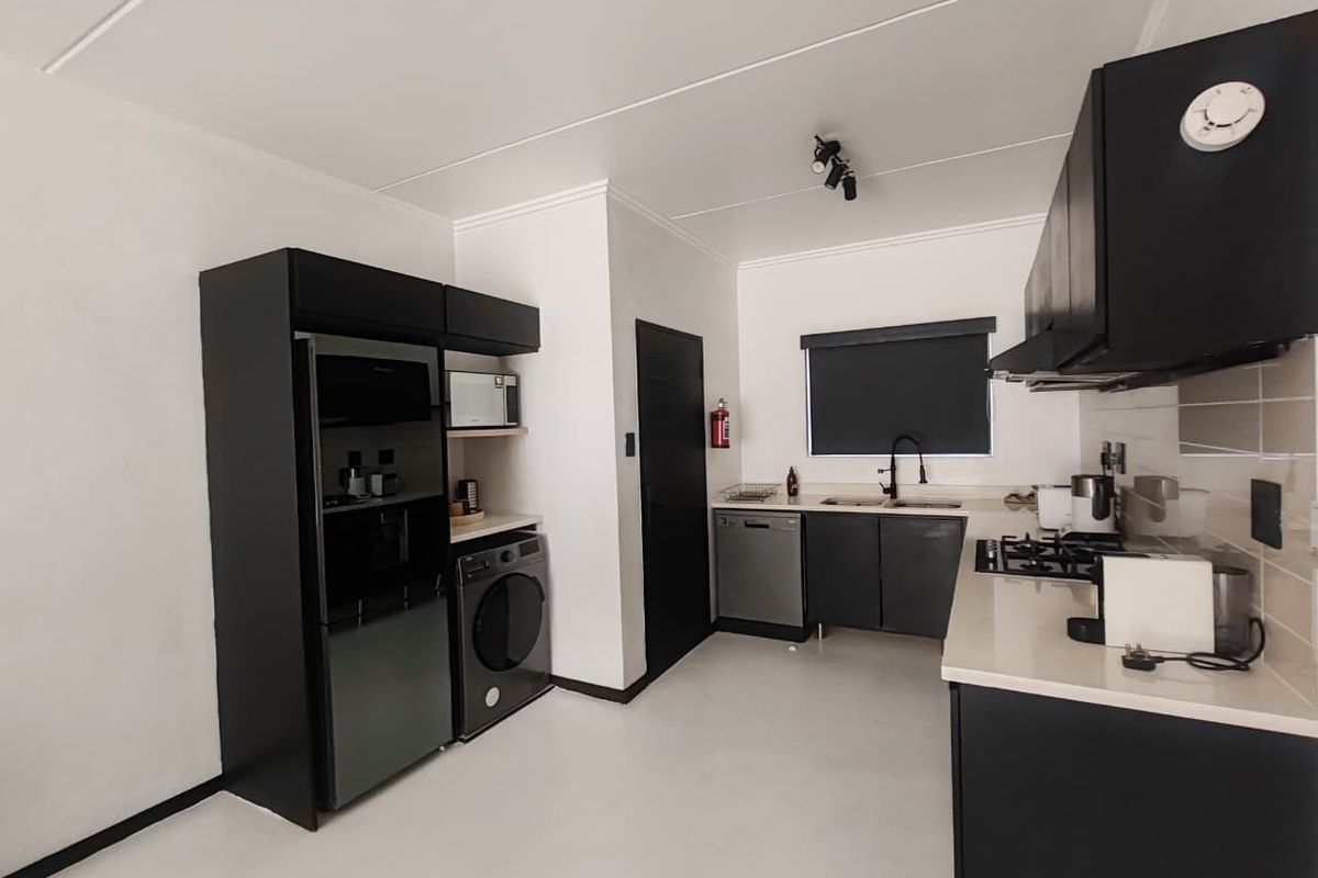 Modern kitchen featuring sleek black cabinetry, stone countertops, a gas hob, extractor fan, and integrated sink with a contemporary mixer tap.