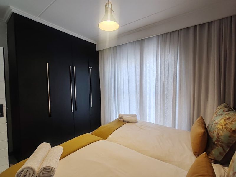 A well-maintained bedroom featuring modern dark built-in cupboards and soft window treatments.