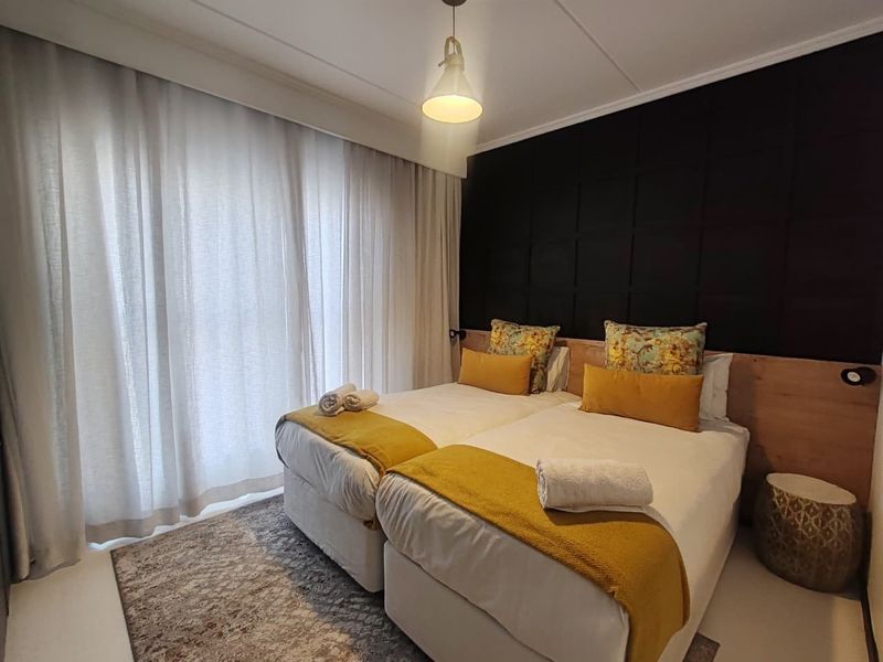 A well-maintained bedroom featuring a modern built-in headboard with integrated lighting and floor-to-ceiling curtains.