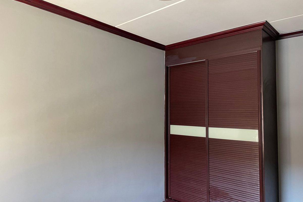 A bedroom featuring a built-in wardrobe with dark wood-tone sliding doors and contrasting decorative ceiling cornicing.