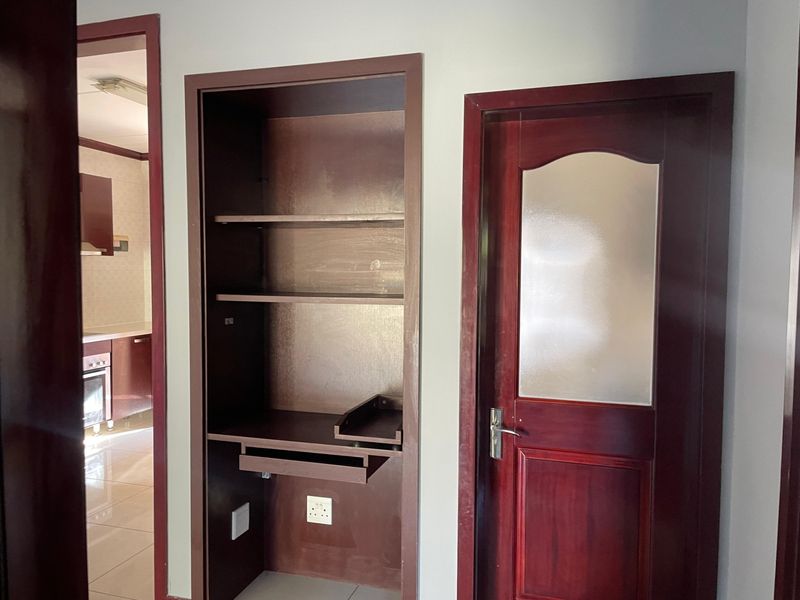 A hallway area featuring a built-in wooden desk and shelving unit, adjacent to a timber door with a frosted glass insert.