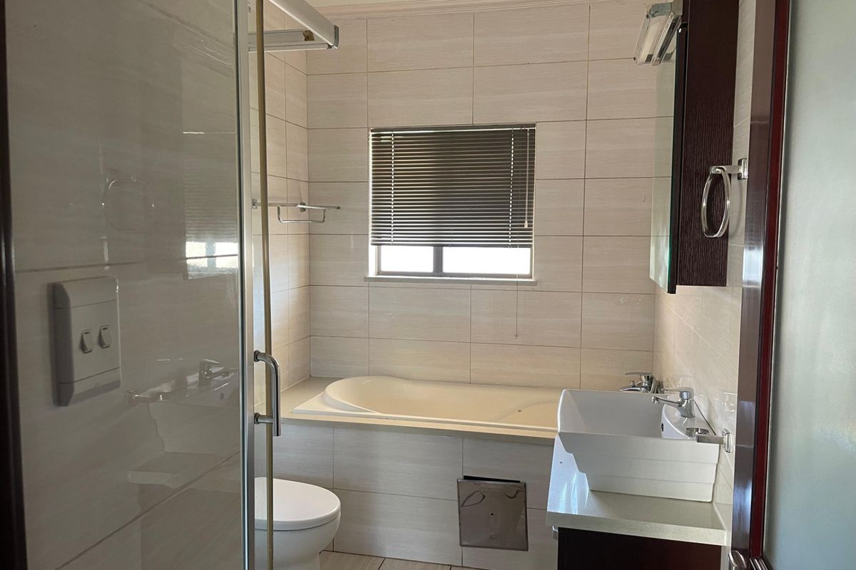 A clean, modern bathroom featuring a built-in bathtub, a separate glass-enclosed shower, and a contemporary vanity basin with storage.