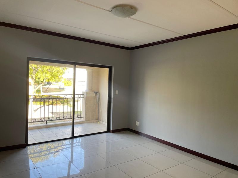 An empty living room featuring neutral grey walls, polished tile flooring, crown molding, and a sliding glass door leading to a private balcony.
