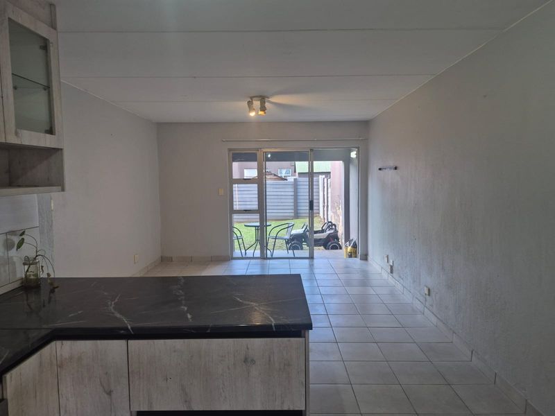 Open-plan living area featuring tiled floors, kitchen cabinetry with marble-look countertops, and a sliding glass door leading to an outdoor space.