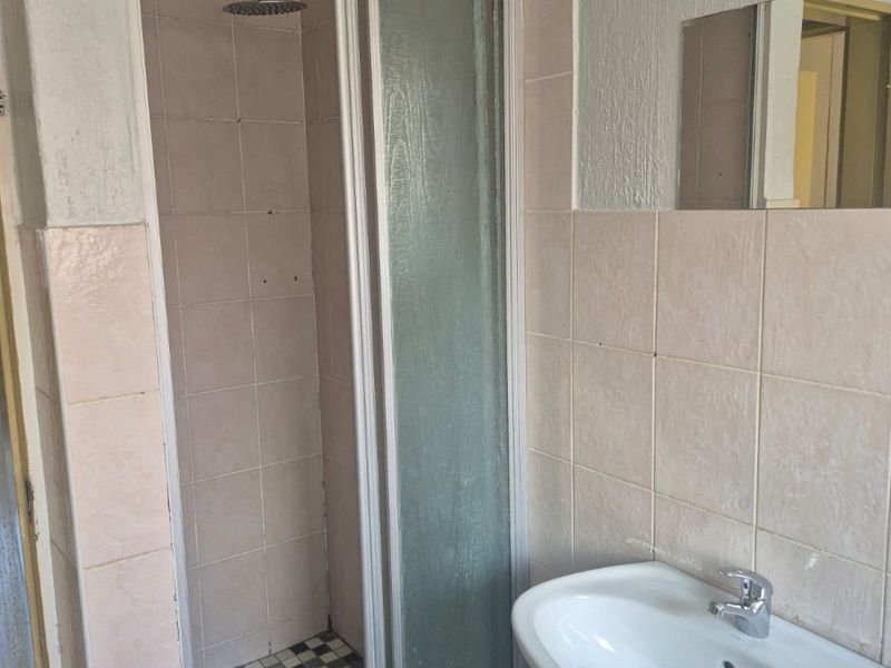 A functional bathroom featuring a shower enclosure with a modern shower head and a pedestal basin with a mixer tap.