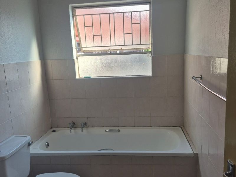 A functional bathroom featuring a built-in bathtub, toilet, and tiled finishes, offering a blank canvas for modern renovation and aesthetic updates.