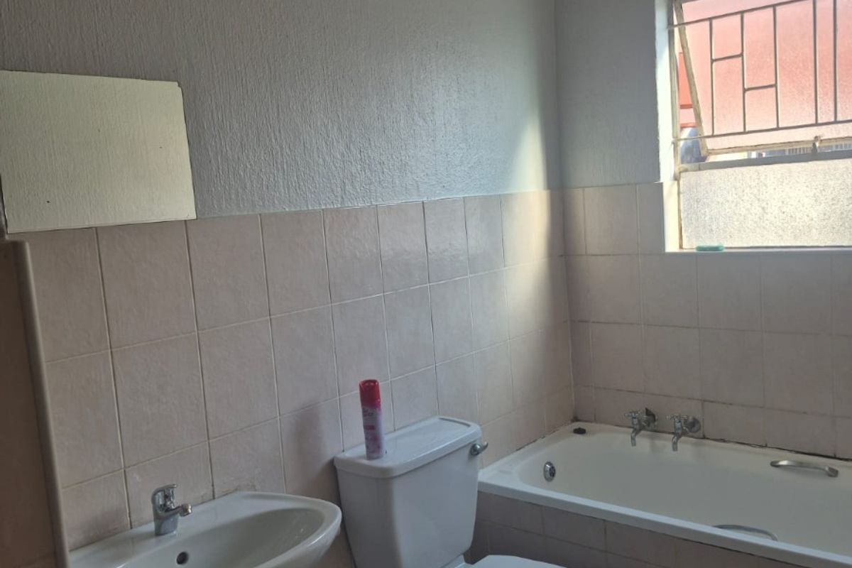 A functional bathroom featuring a pedestal basin, toilet, and built-in bathtub with tiled finishes and security bars on the window.