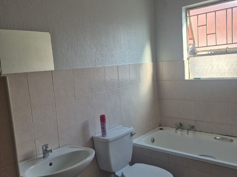 A functional bathroom featuring a pedestal basin, toilet, and built-in bathtub with tiled finishes and security bars on the window.