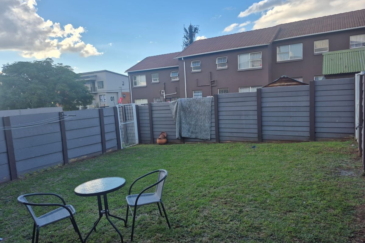 A private rear garden featuring a lawn area enclosed by a precast concrete boundary wall and a secure metal gate.