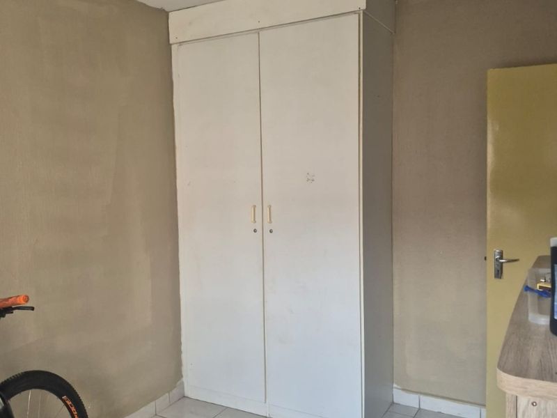 A bedroom featuring a built-in wardrobe, tiled flooring, and neutral wall paint, offering a blank canvas for potential interior updates.
