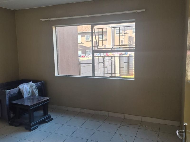A simple bedroom featuring tiled flooring, a window with security bars, and neutral wall paint, offering a blank canvas for potential interior updates.
