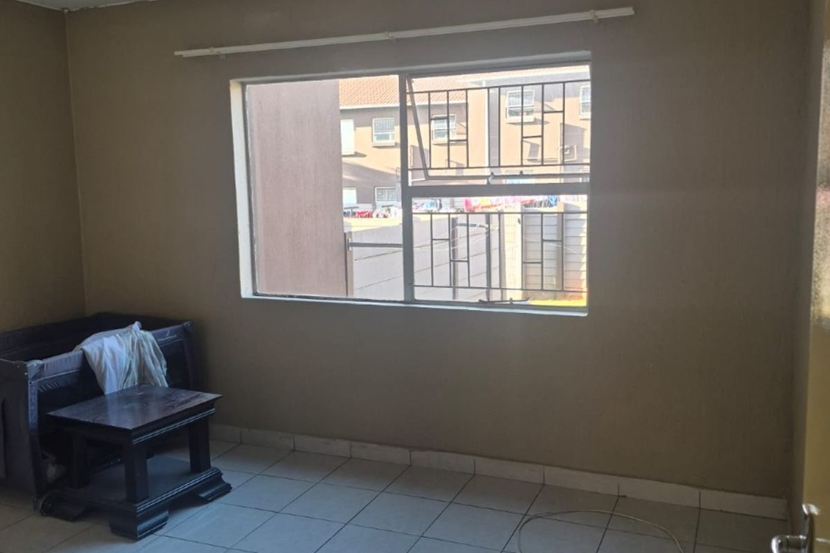 A simple bedroom featuring tiled flooring, a window with security bars, and neutral wall paint, offering a blank canvas for potential interior updates.