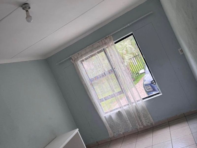 A simple, empty bedroom featuring tiled flooring and a window, providing a blank canvas for potential interior design updates.