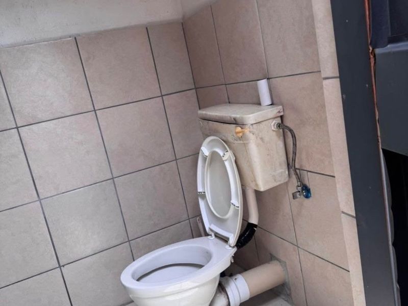 A small bathroom featuring tiled walls and flooring with a standard toilet and exposed plumbing fixtures.
