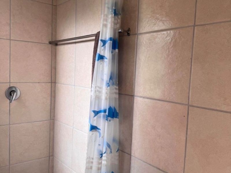 A functional bathroom shower area featuring tiled walls, a wall-mounted basin, and a shower fixture.