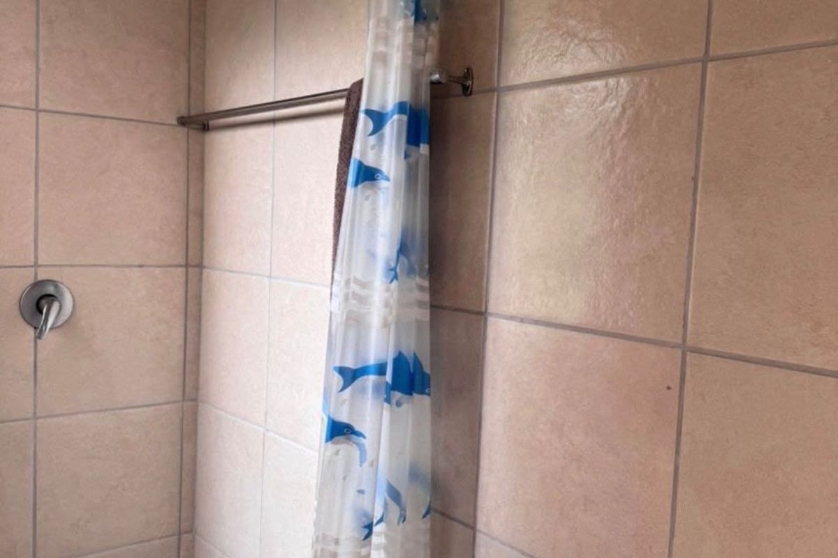 A functional bathroom shower area featuring tiled walls, a wall-mounted basin, and a shower fixture.