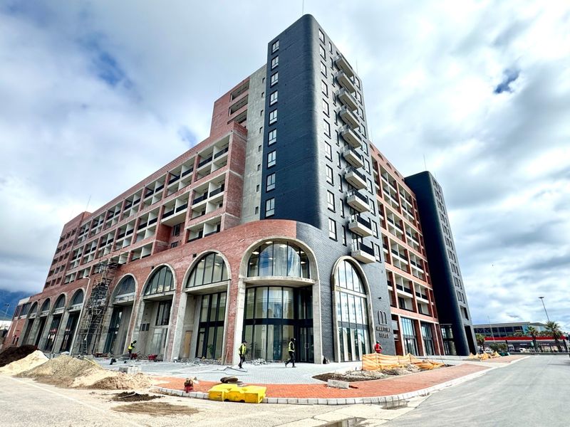 A modern multi-story residential building under construction, featuring a distinctive brick facade, arched ground-floor windows, and multiple balconies.