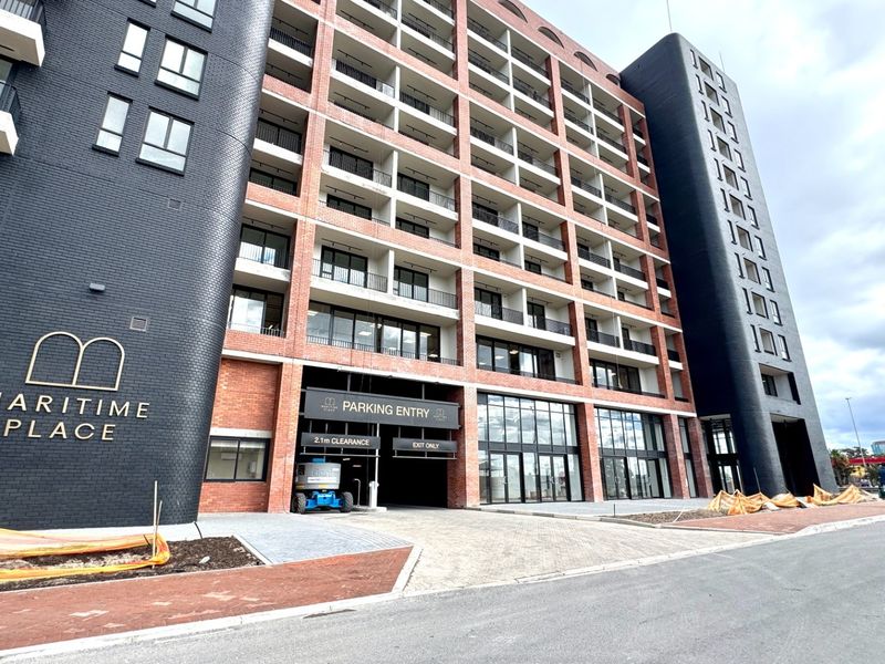 Modern multi-story apartment building facade featuring brickwork, private balconies, and a dedicated parking entrance at street level.