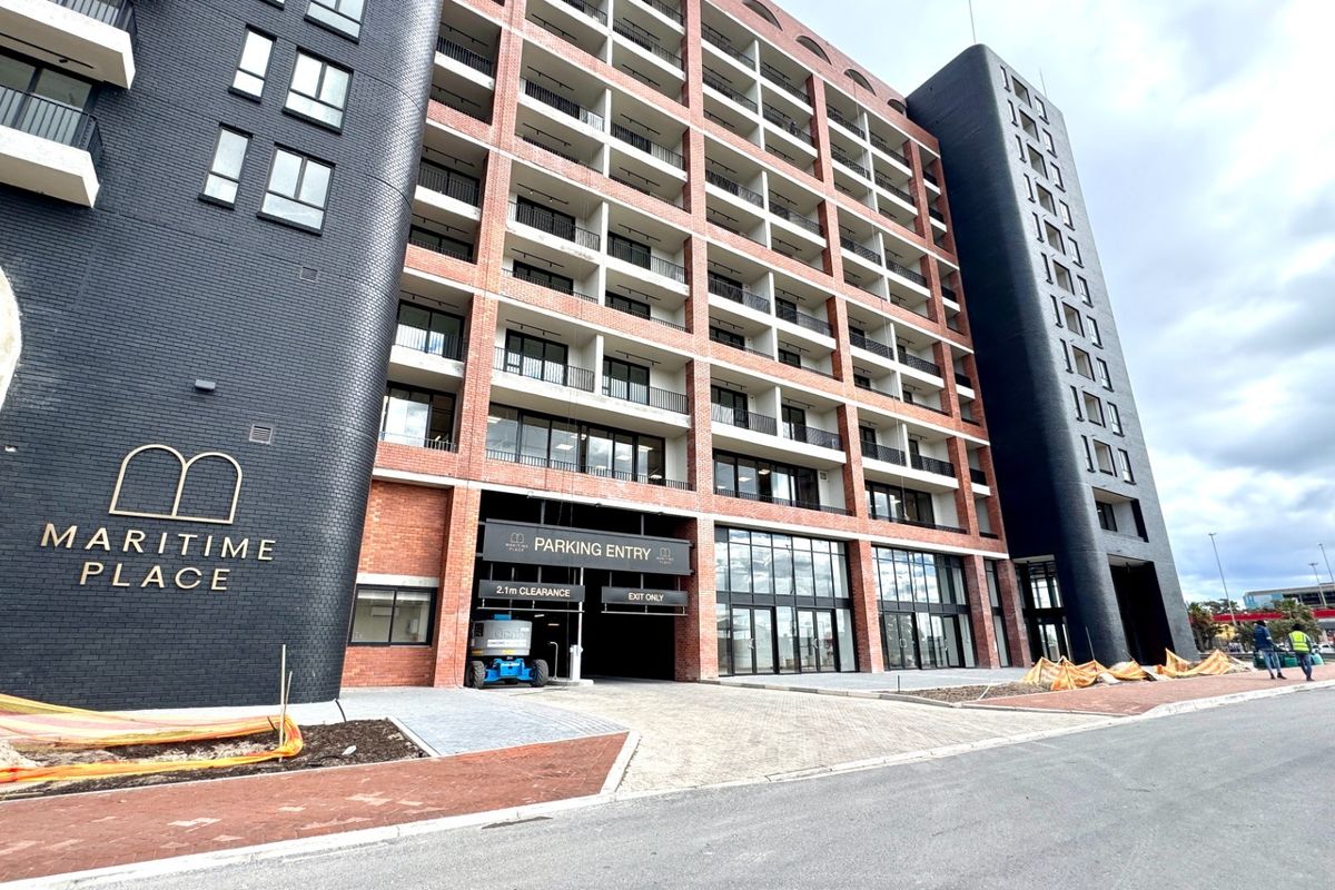 Modern multi-story apartment building facade featuring brickwork, private balconies, and a dedicated parking entrance at street level.
