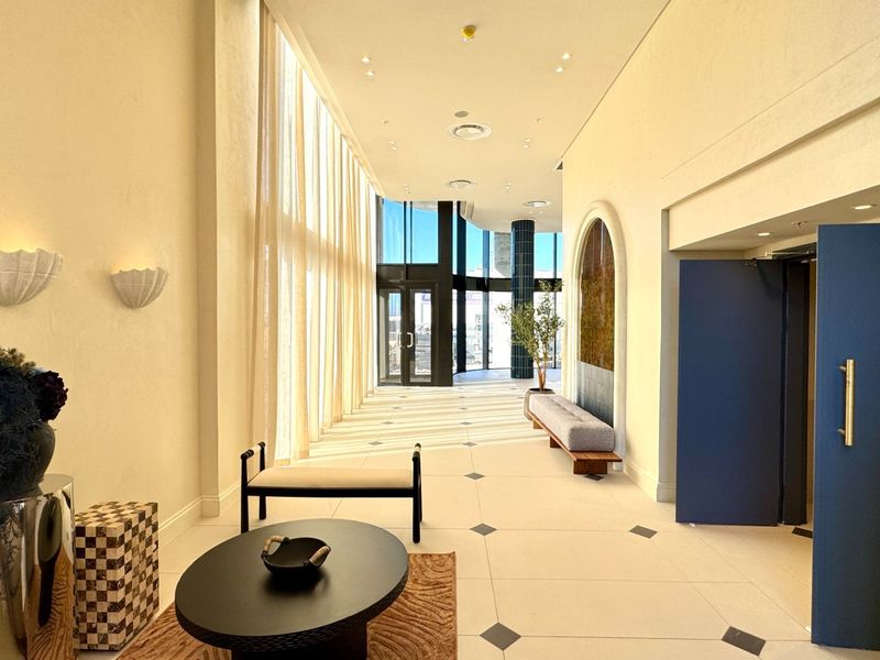 A spacious and elegant entrance hall featuring high ceilings, large windows, tiled flooring with decorative inlays, and a sophisticated arched wall feature.