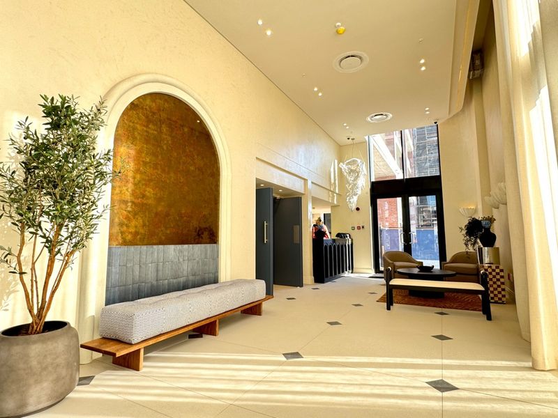 A bright and elegant entrance foyer featuring high ceilings, large windows, tiled flooring with decorative inlays, and a striking arched feature wall.