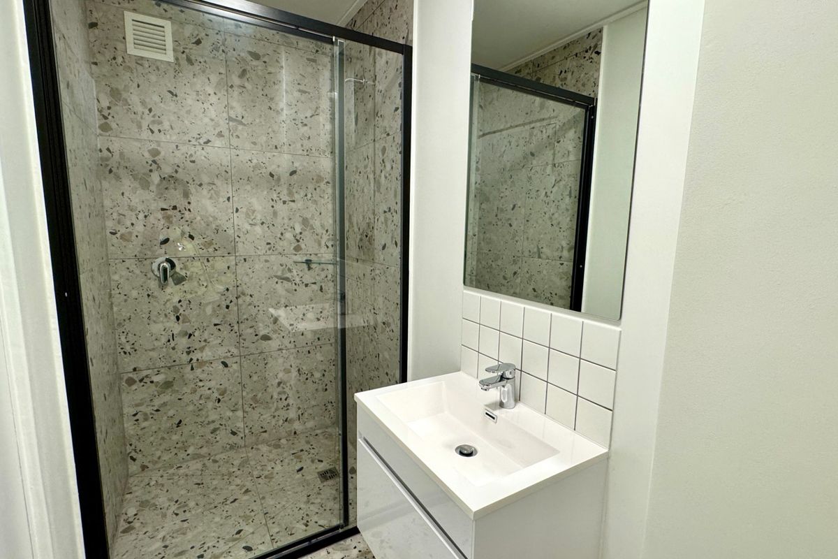 Modern bathroom featuring a glass-enclosed shower with terrazzo-style tiling, a sleek wall-mounted vanity with integrated basin, and a clean, contemporary aesthetic.