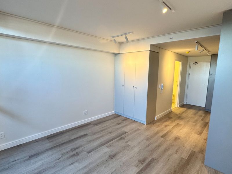 A bright, empty bedroom featuring modern laminate flooring, built-in cupboards, and adjustable track lighting, offering a clean and neutral space ready for personalization.