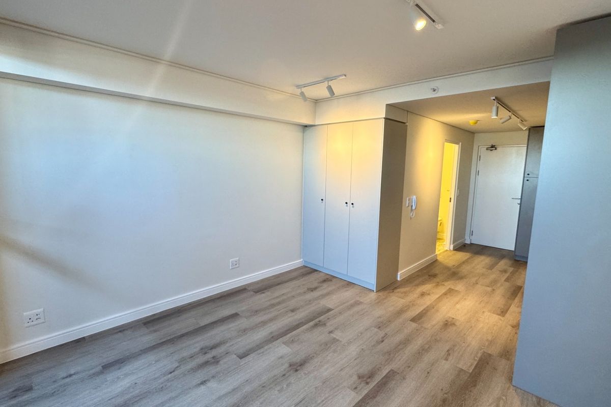 A bright, empty bedroom featuring modern laminate flooring, built-in cupboards, and adjustable track lighting, offering a clean and neutral space ready for personalization.