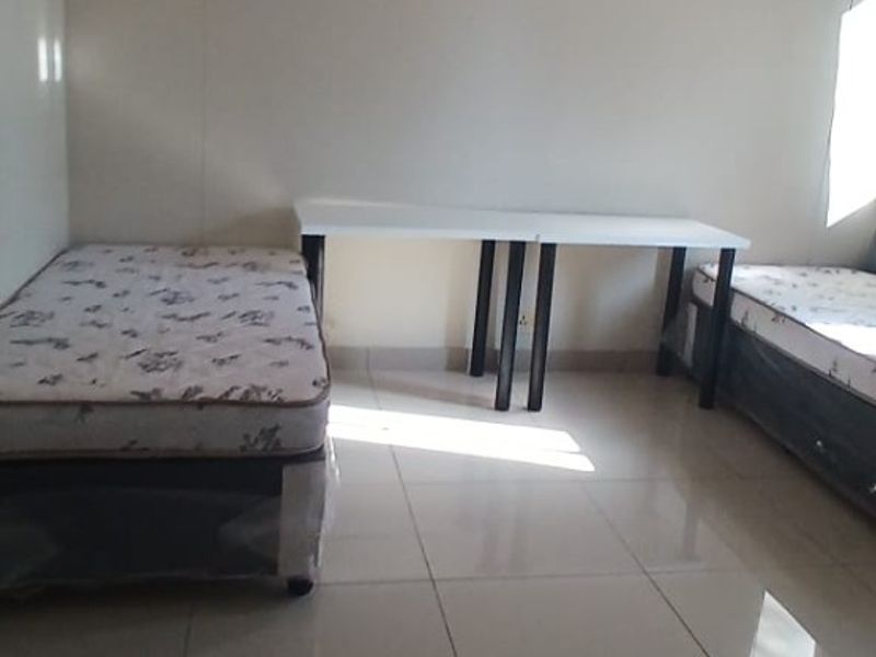 A simple bedroom featuring neutral walls and tiled flooring, providing a functional and clean space.