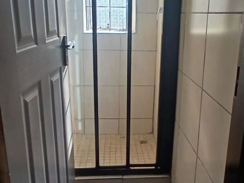 A compact bathroom featuring a shower enclosure with tiled walls and flooring, including a window with security bars.