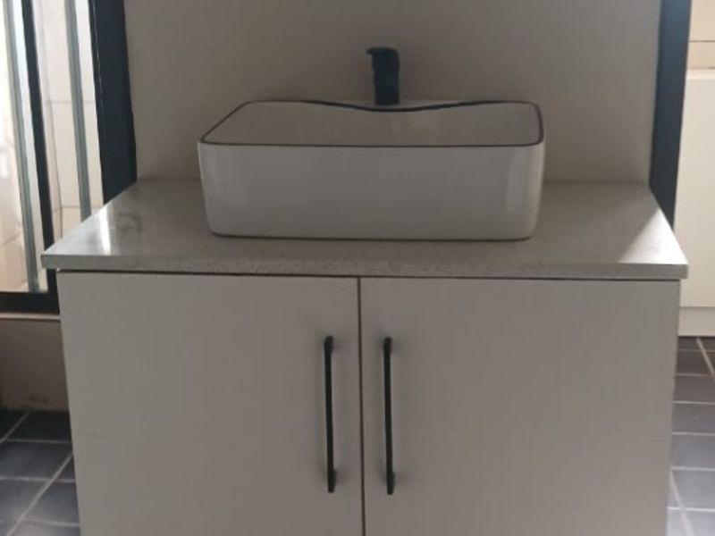 A modern bathroom vanity featuring a white cabinet, stone-look countertop, and a rectangular vessel sink with a black faucet.