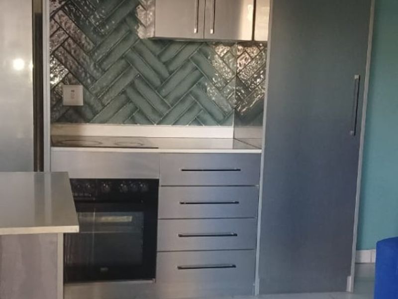Modern kitchen featuring sleek grey cabinetry, a stylish herringbone tile backsplash, built-in oven and hob, and polished marble-look floor tiles.
