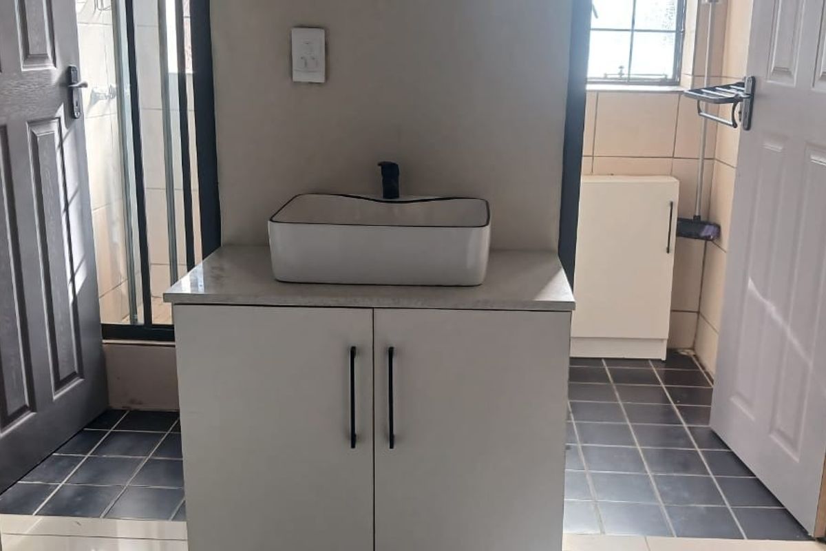 A clean bathroom featuring a modern vessel sink on a white vanity cabinet with dark tiled flooring and neutral wall finishes.