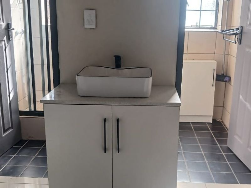 A clean bathroom featuring a modern vessel sink on a white vanity cabinet with dark tiled flooring and neutral wall finishes.