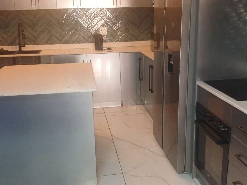 Modern kitchen featuring a central island, stone countertops, herringbone tile backsplash, built-in oven, electric hob, and sleek fitted cabinetry with porcelain floor tiles.